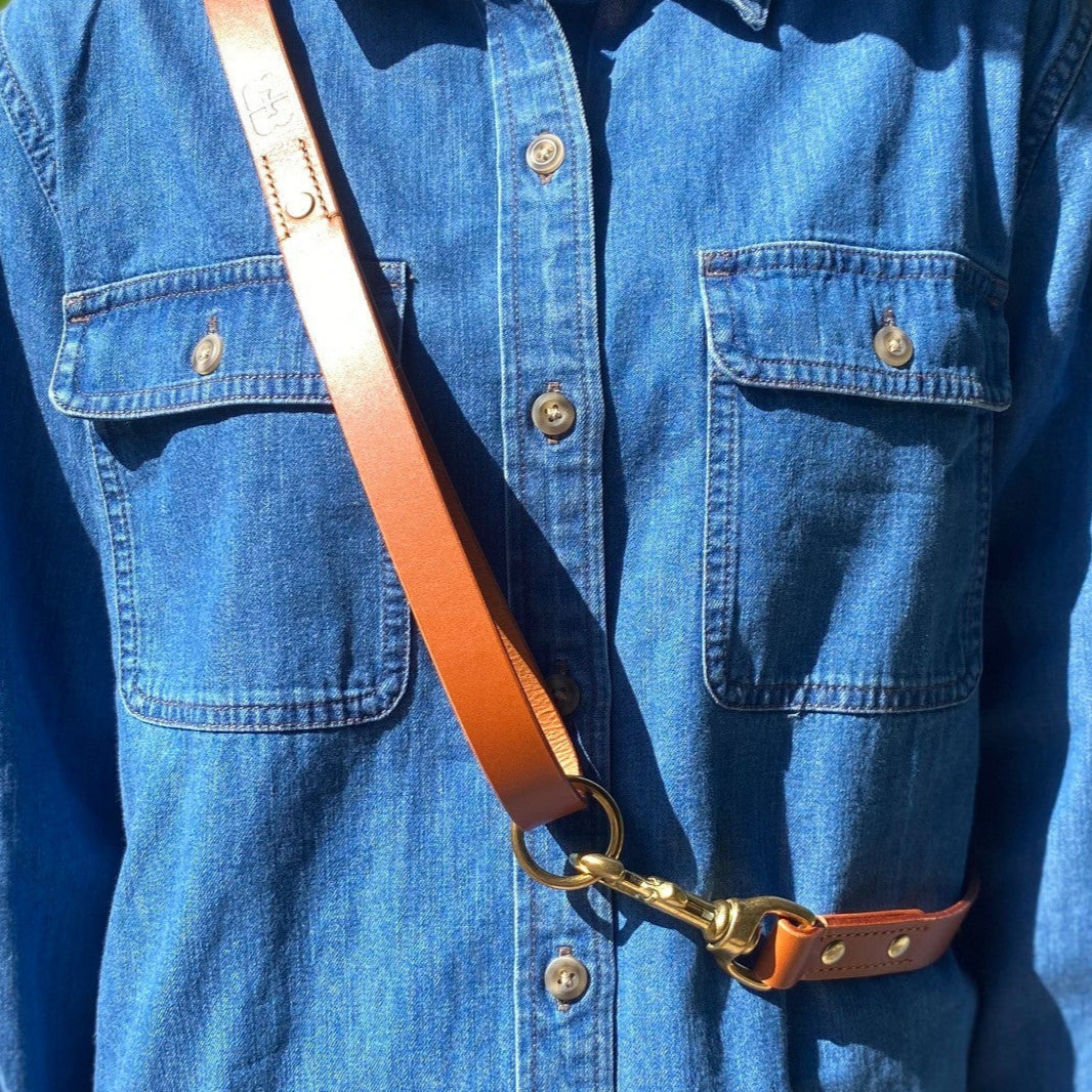 Person wearing a blue denim shirt with a brown leather lead over the shoulder.