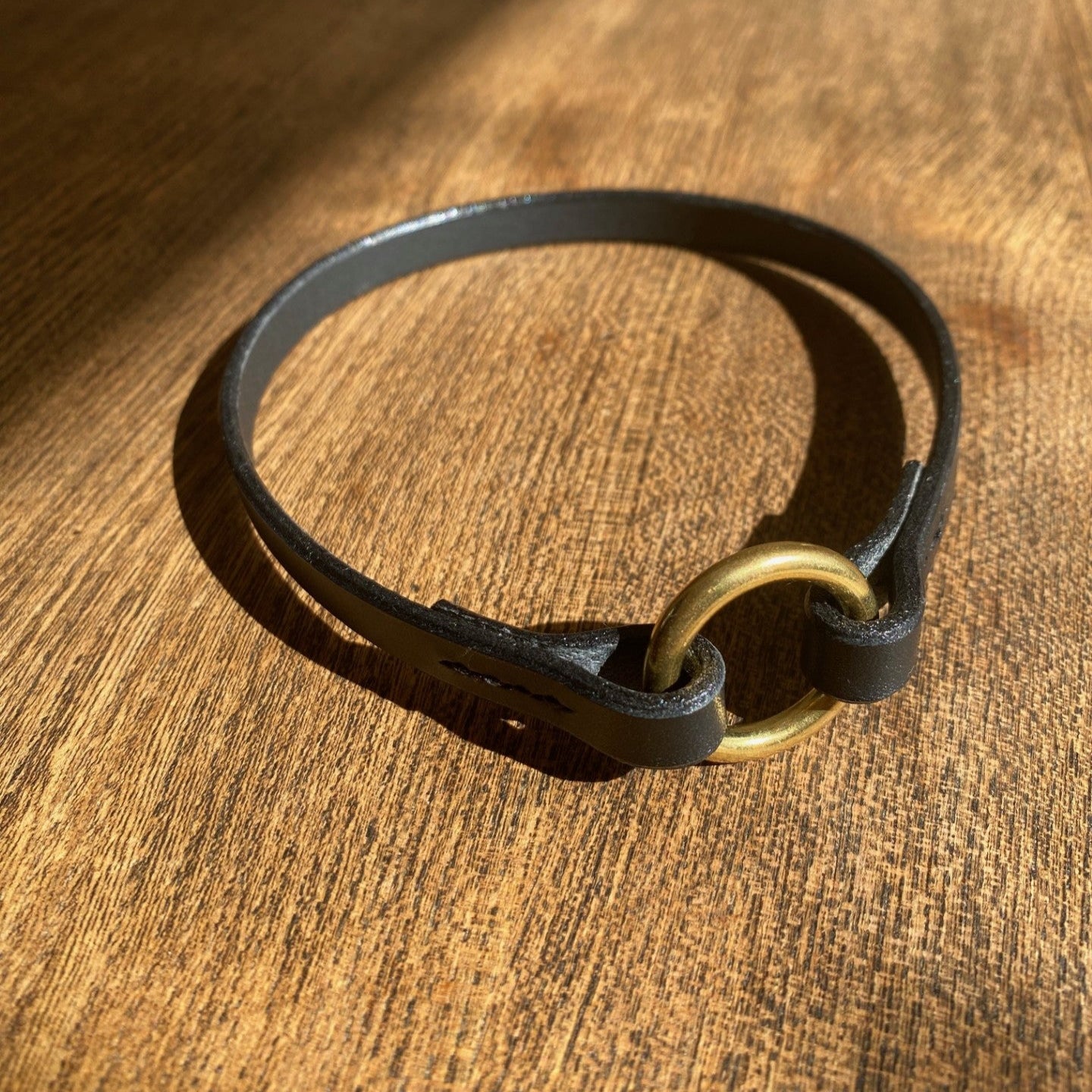 Black leather thin collar with a gold ring on a wooden surface