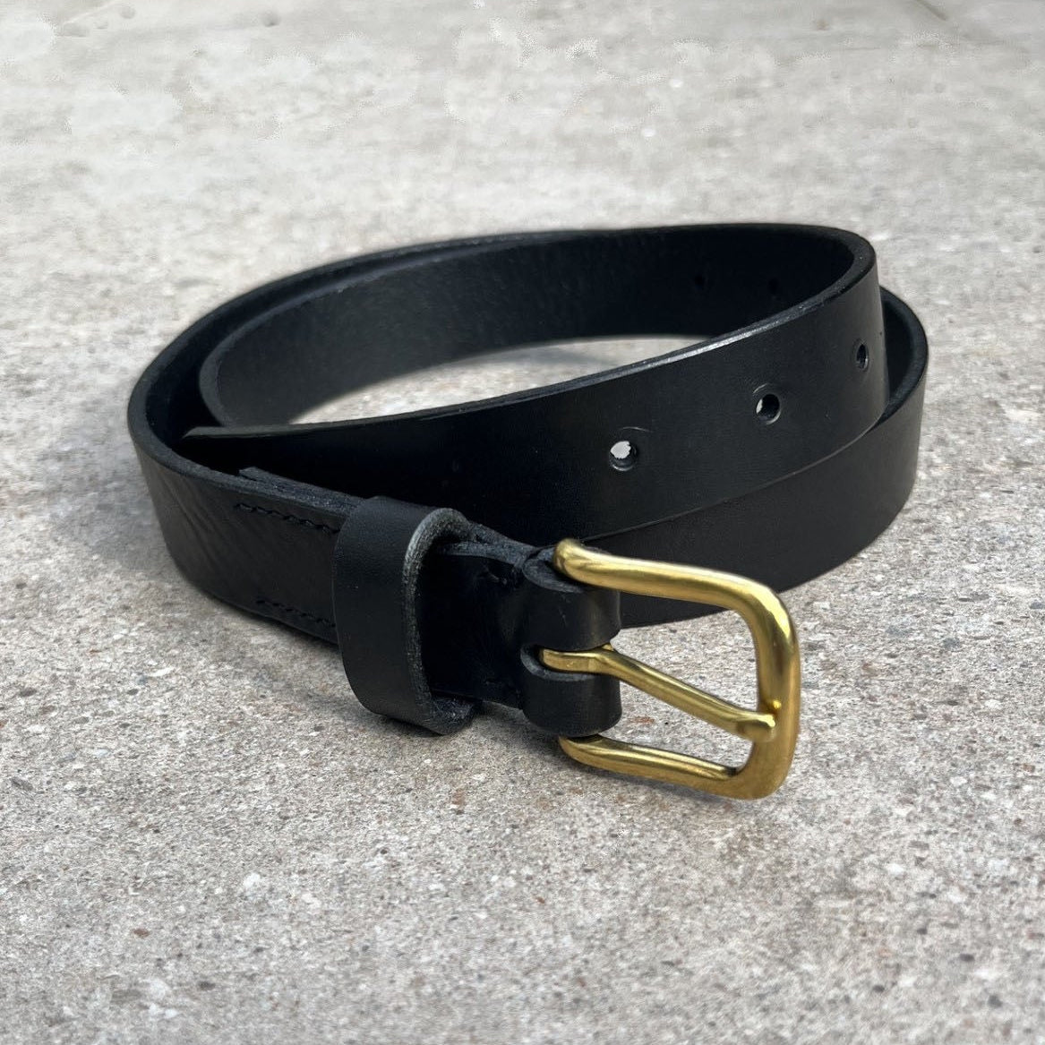 Coiled black belt with a brass buckle on a stone surface