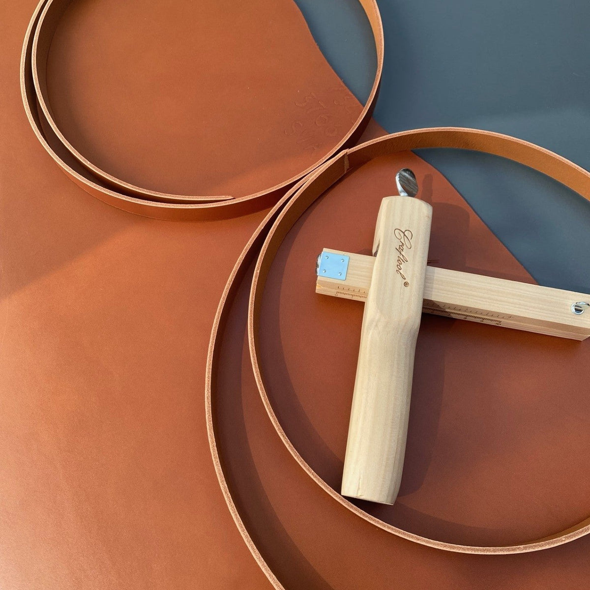 A piece of tan leather with a strap cutter and leather strips