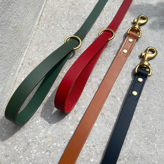 Four dog leashes in green, red, brown, and black on a stone surface.