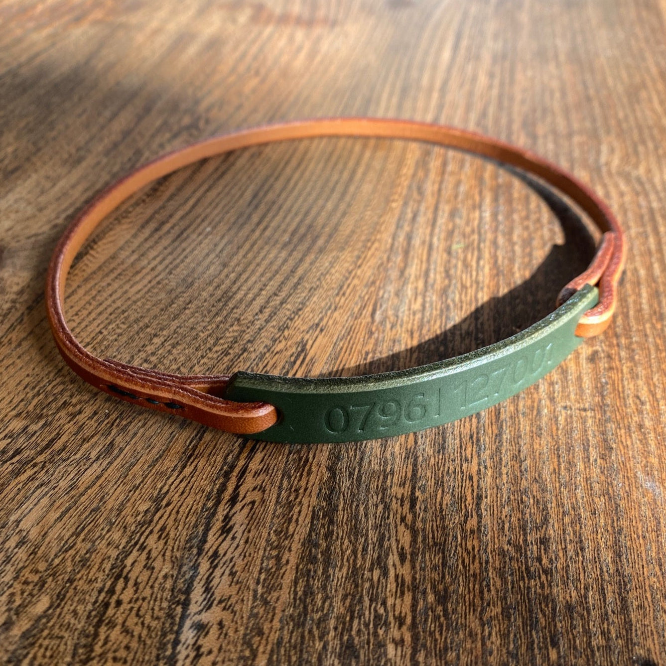 Green and tan leather dog house collar on a wooden surface