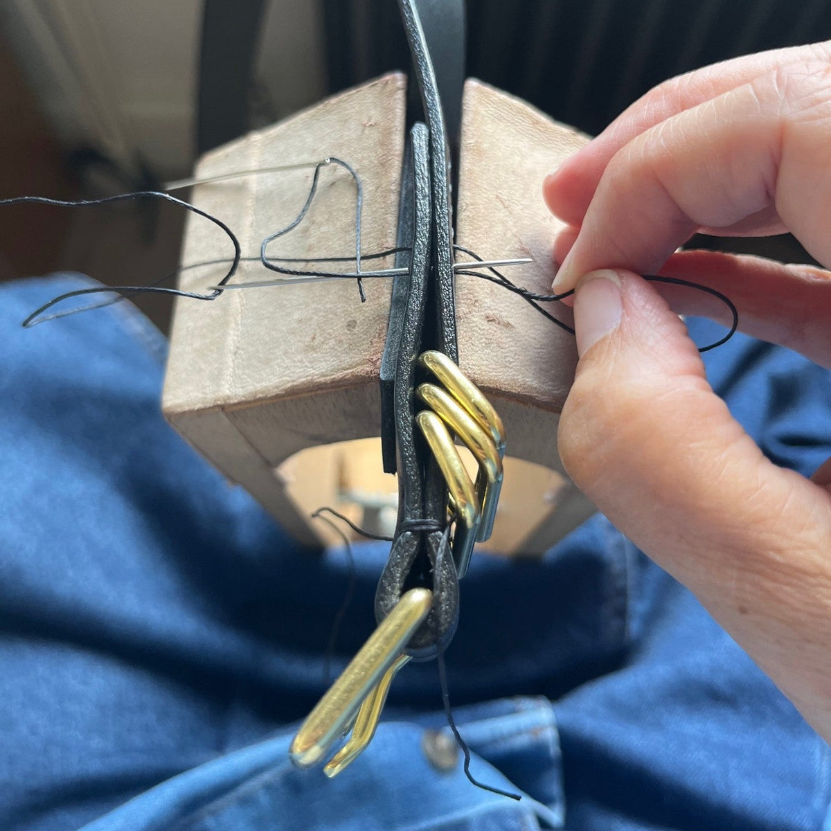 A close-up of a hand sewing a black leather belt with gold-colored metal.