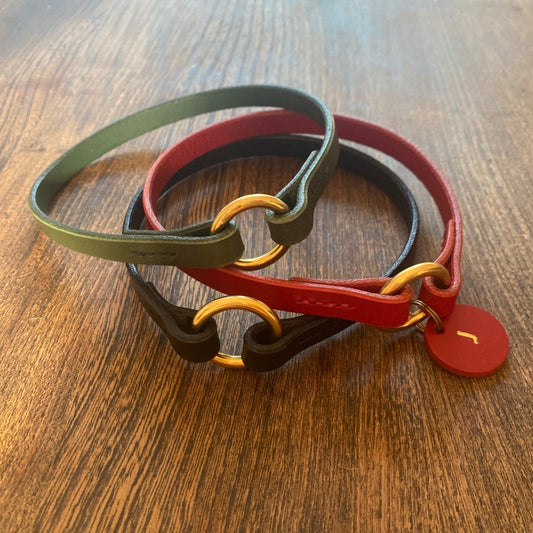 Three thin dog collars in different colours on a wooden surface