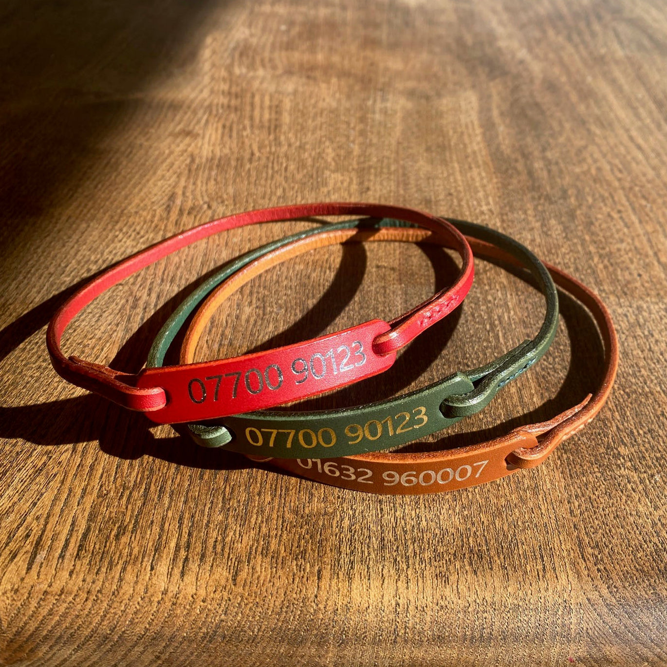 Three dog house collars in red, green, and brown on a wooden surface.
